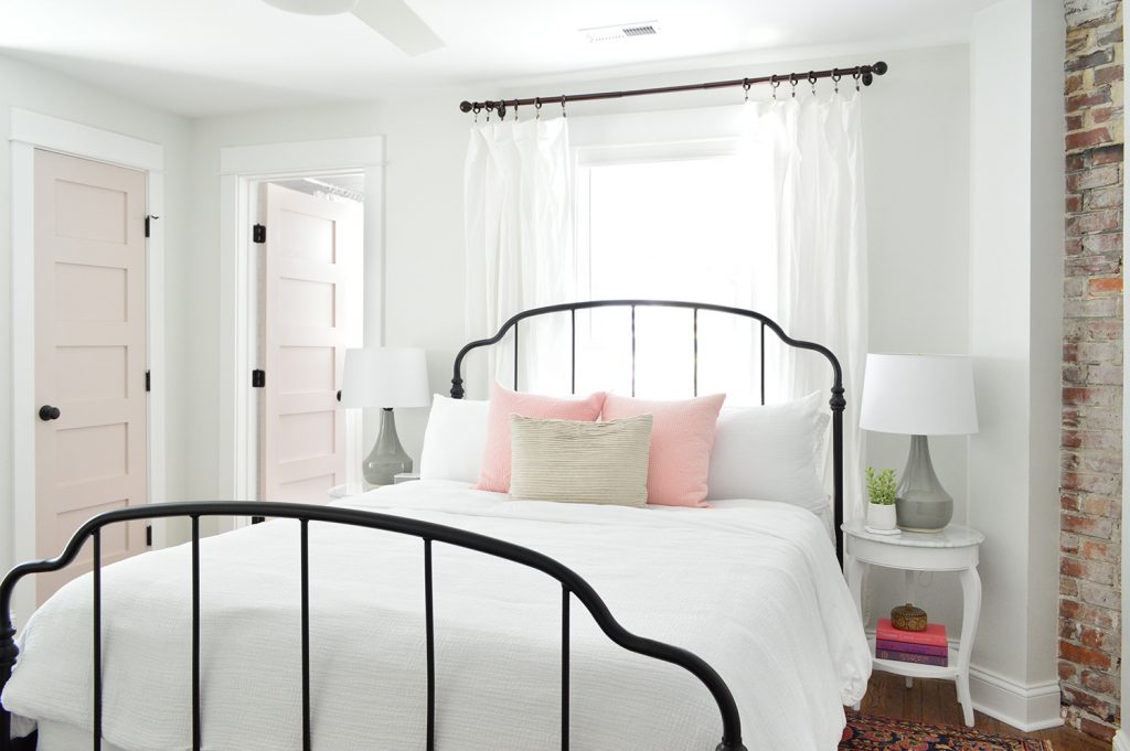 Main Bedroom In Historic Duplex Beach House With Exposed Brick Fireplace | Iron Bedframe | Pink White Truffle Doors