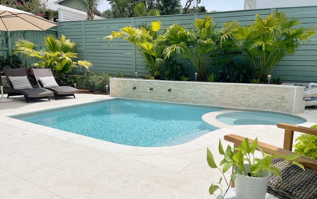 Small backyard pool with curved edge and fan palm plants behind retaining wall